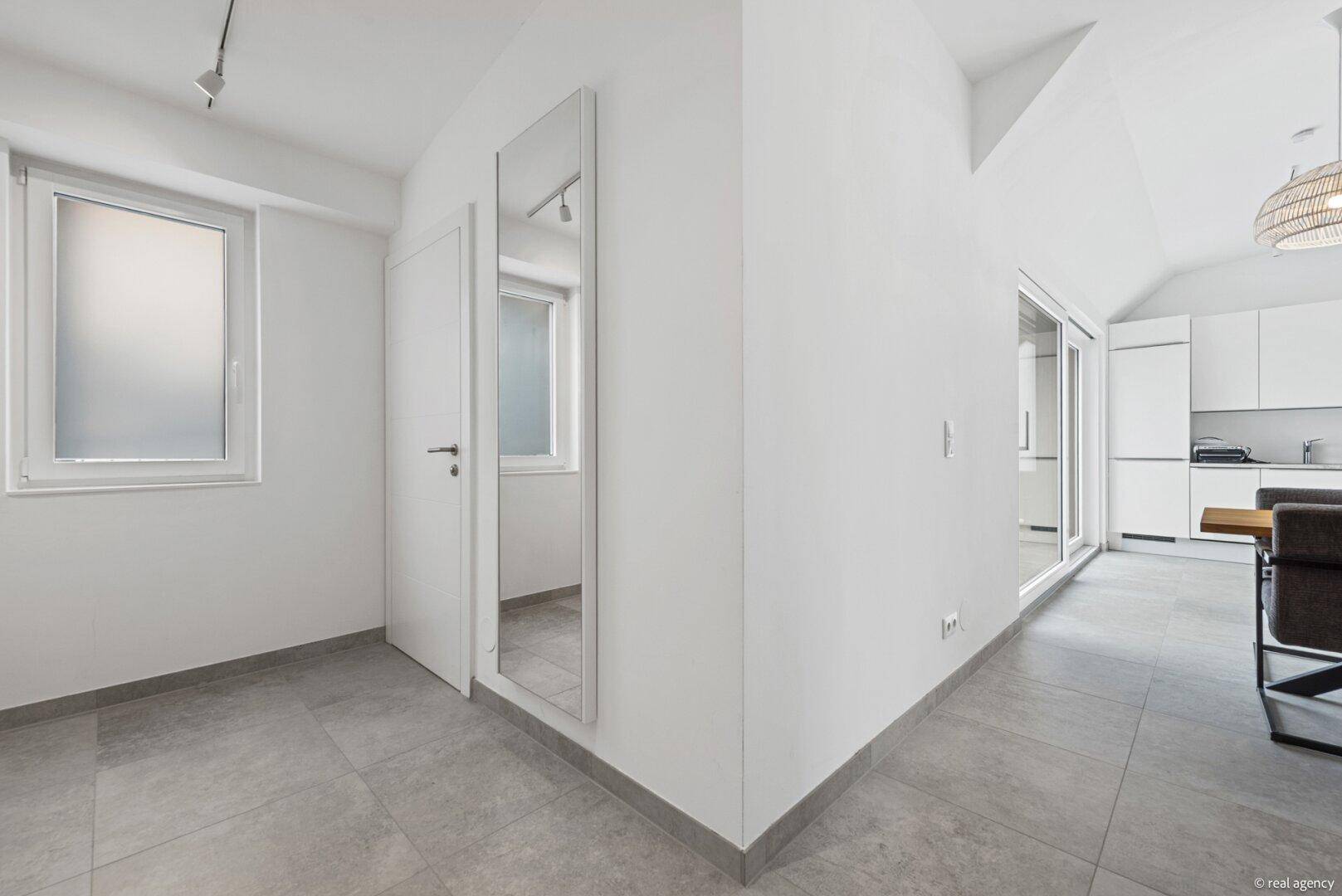 Heller Bereich mit Fliesenboden, Fenster und Übergang zu anderen Räumen.