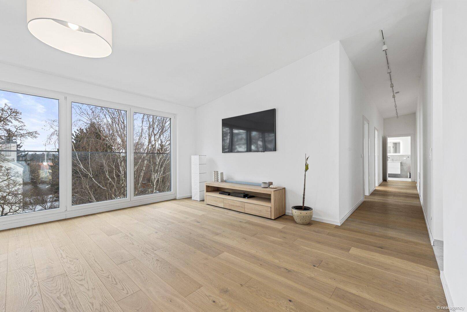 Geräumiges Wohnzimmer mit großen Fenstern, Holzboden und Blick ins Grüne.
