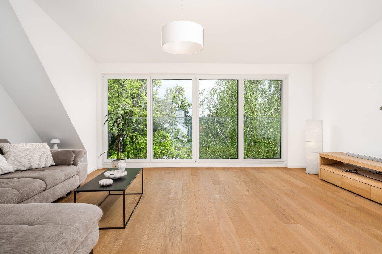 Lichtdurchflutetes Wohnzimmer mit Holzboden, bequemer Couch und weitem Blick ins Grüne.