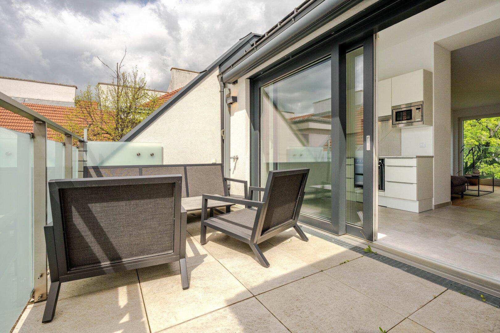Sonniger Terrassenbereich mit Schiebetür zur Küche und modernen Sitzgelegenheiten.