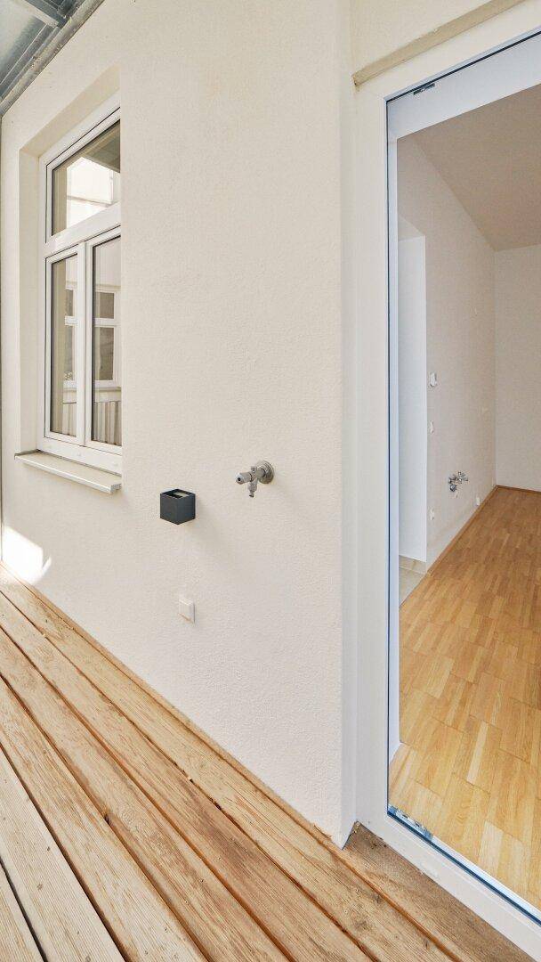 Balkon mit Holzbelag und weißer Wand, ausgestattet mit einem praktischen Außenwasserhahn.