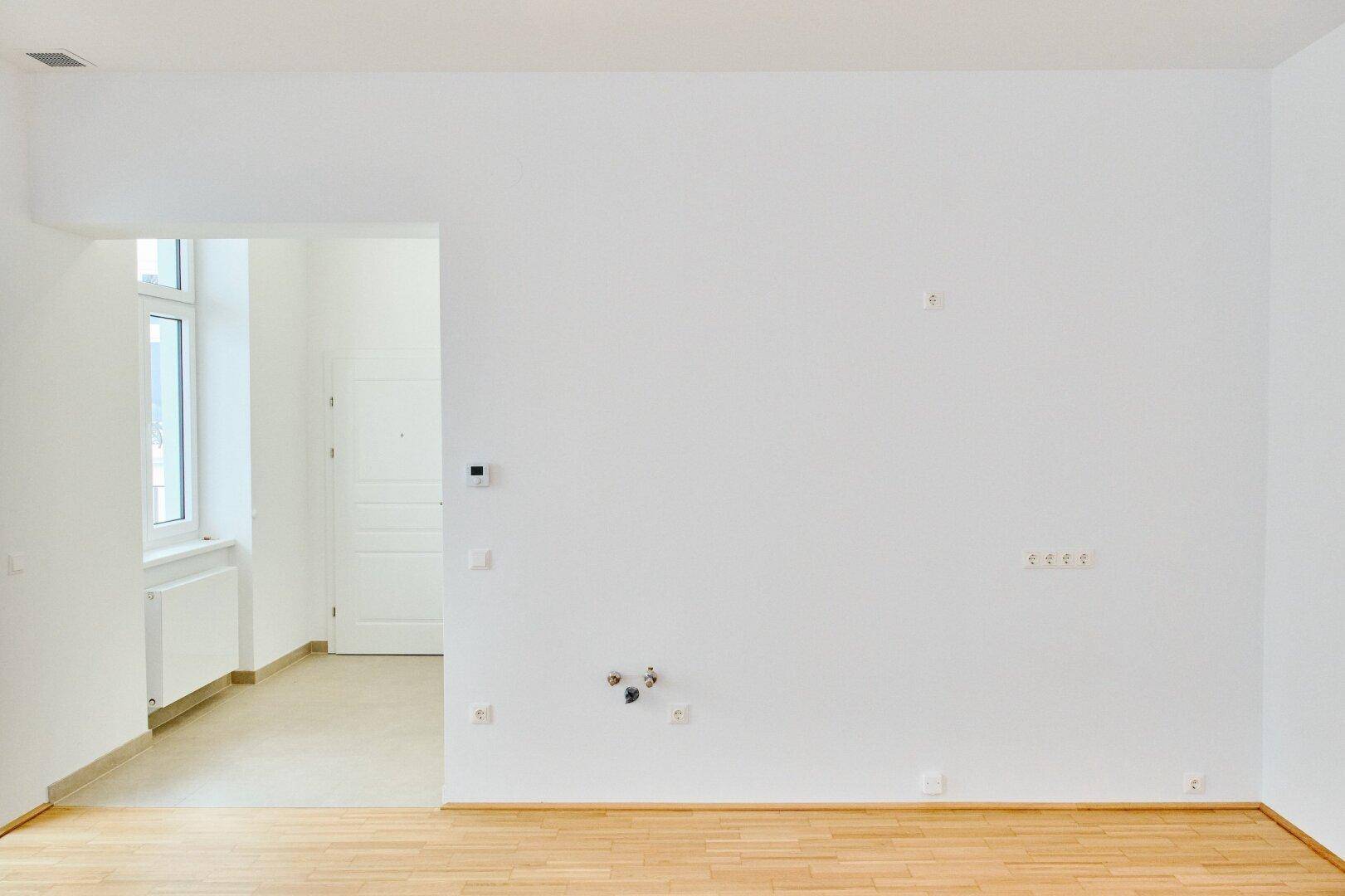 Leerer Raum mit Parkettboden und weißen Wänden, vorbereitet für die Installation einer Küche oder eines Hauswirtschaftsraums.
