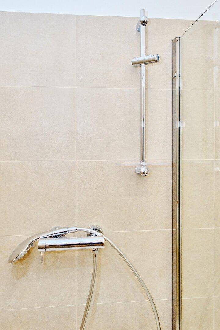Moderne Duscharmaturen mit Handbrause und Duschstange an beigefarbenen Fliesen, in neuwertigem Zustand.