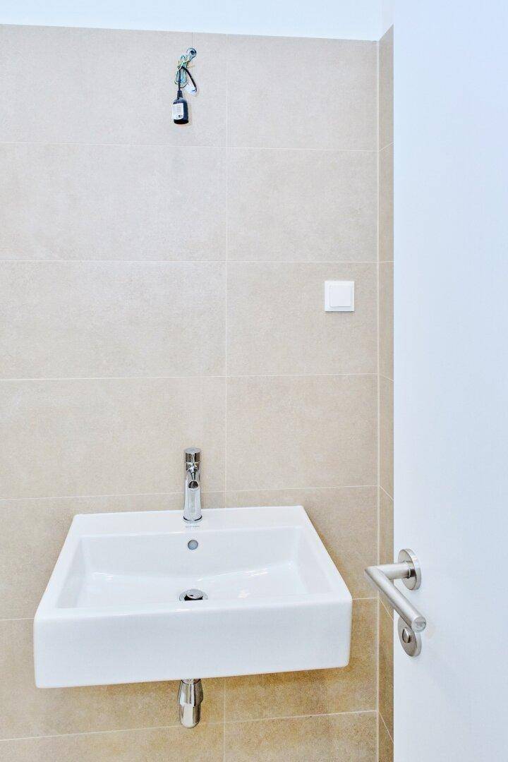 Modernes rechteckiges Waschbecken mit Chromarmatur vor beigefarbenen Fliesen, minimalistisch und funktional.