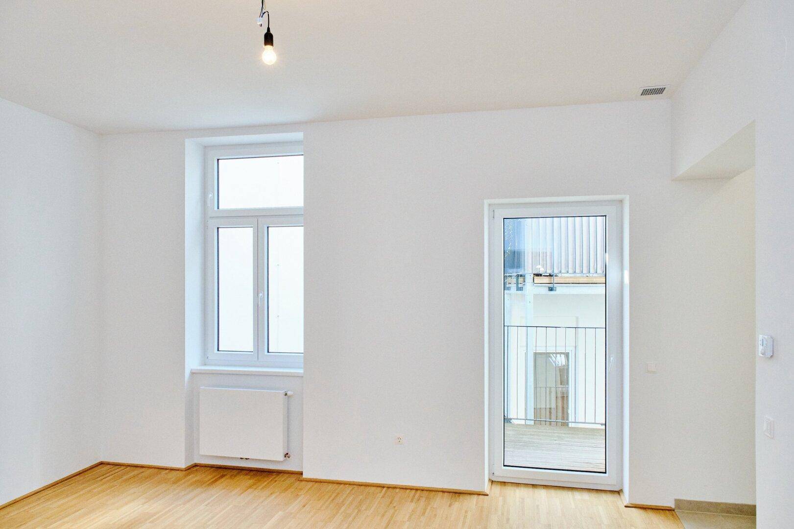 Heller Raum mit Parkettboden und Zugang zu einem Balkon, ideal für ein Wohn- oder Schlafzimmer.