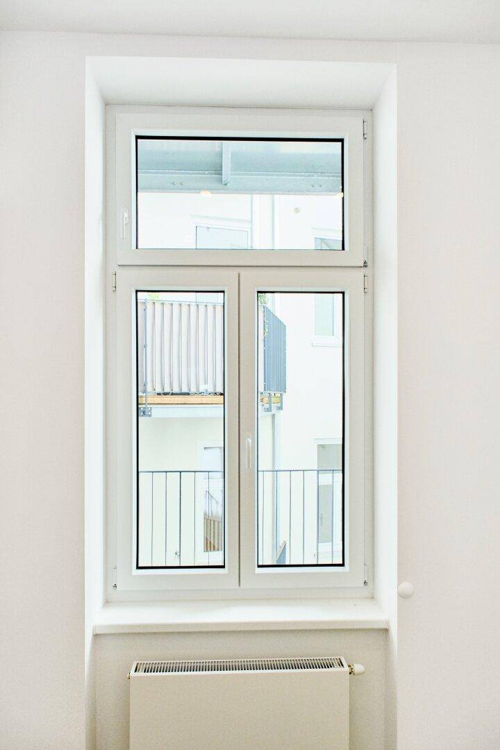Großes Fenster mit Blick auf den Innenhof, darunter ein Heizkörper, in einem hellen Raum.