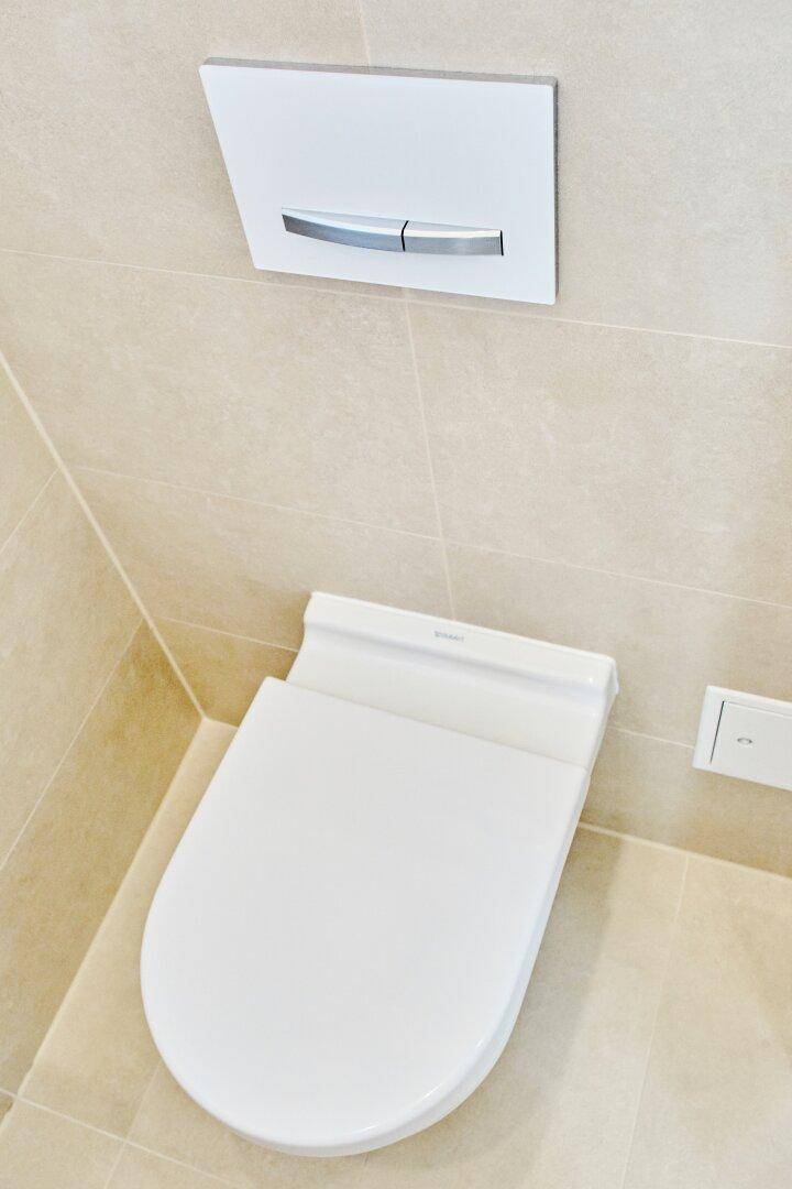 Modernes Wand-WC mit Spülkasten und beigefarbenen Fliesen an Wänden und Boden.