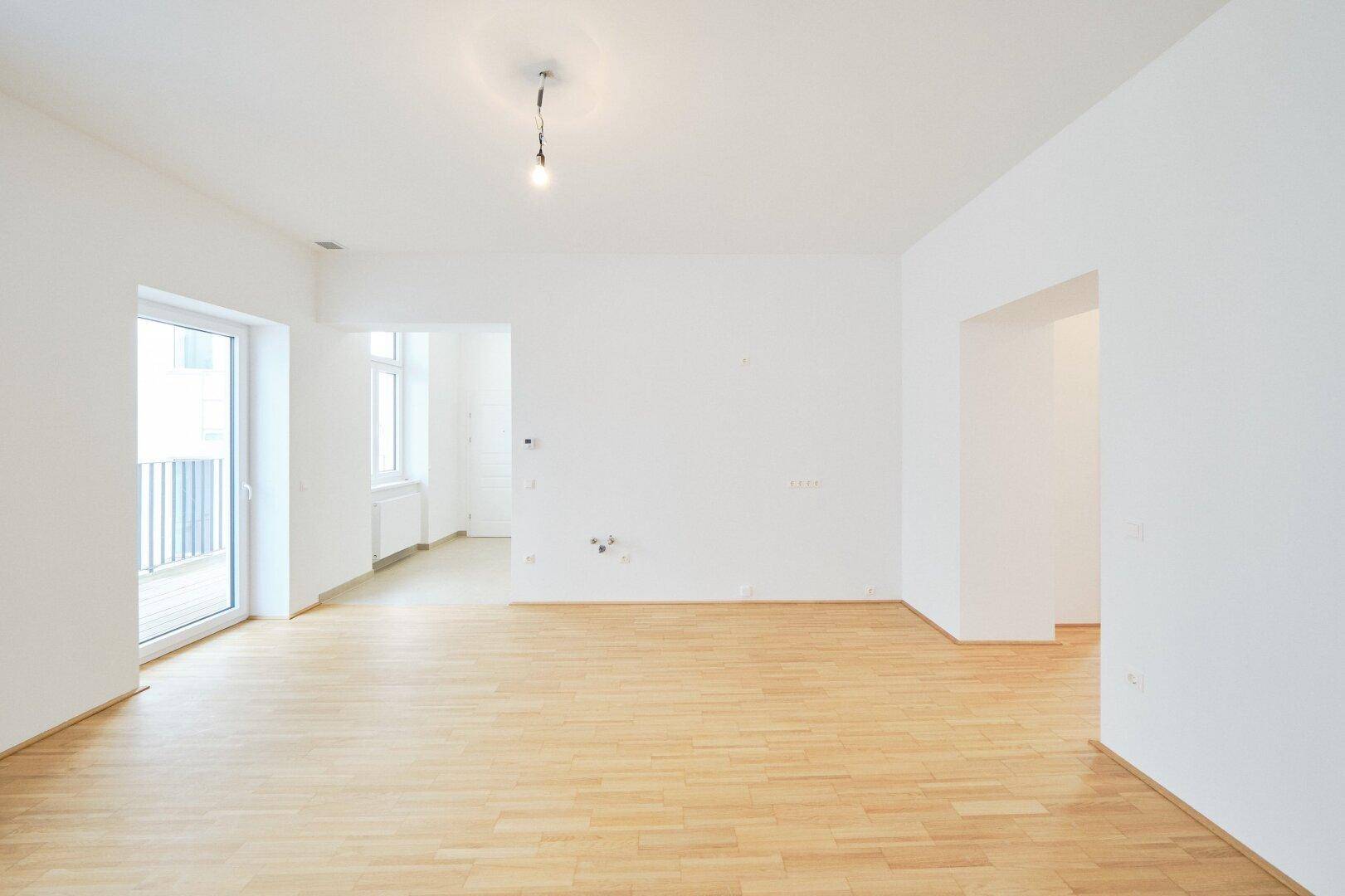 Heller Wohnbereich mit Parkettboden und direktem Zugang zu einem Balkon.