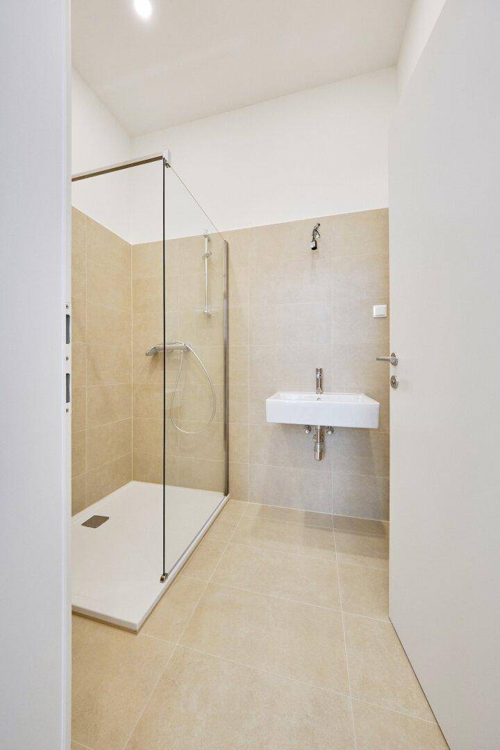 Modernes Badezimmer mit begehbarer Dusche, Wandwaschbecken und hellen Fliesen.