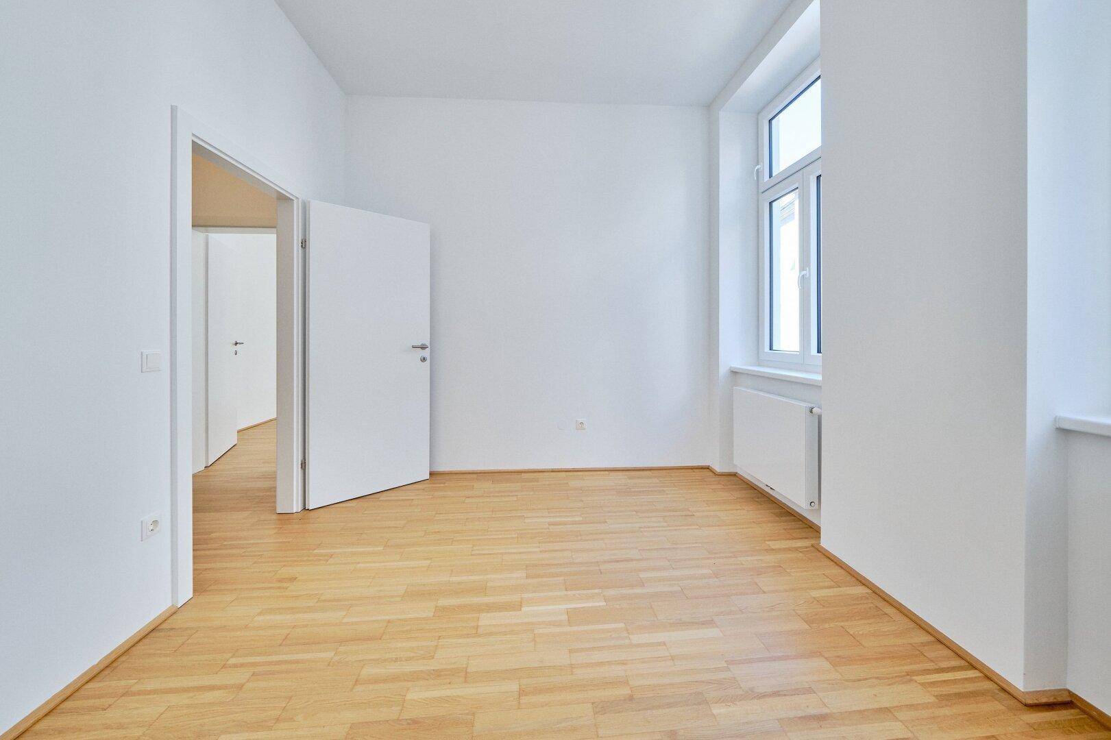 Unmöbliertes Zimmer mit Parkettboden und großem Fenster, ideal als Schlaf- oder Arbeitszimmer.