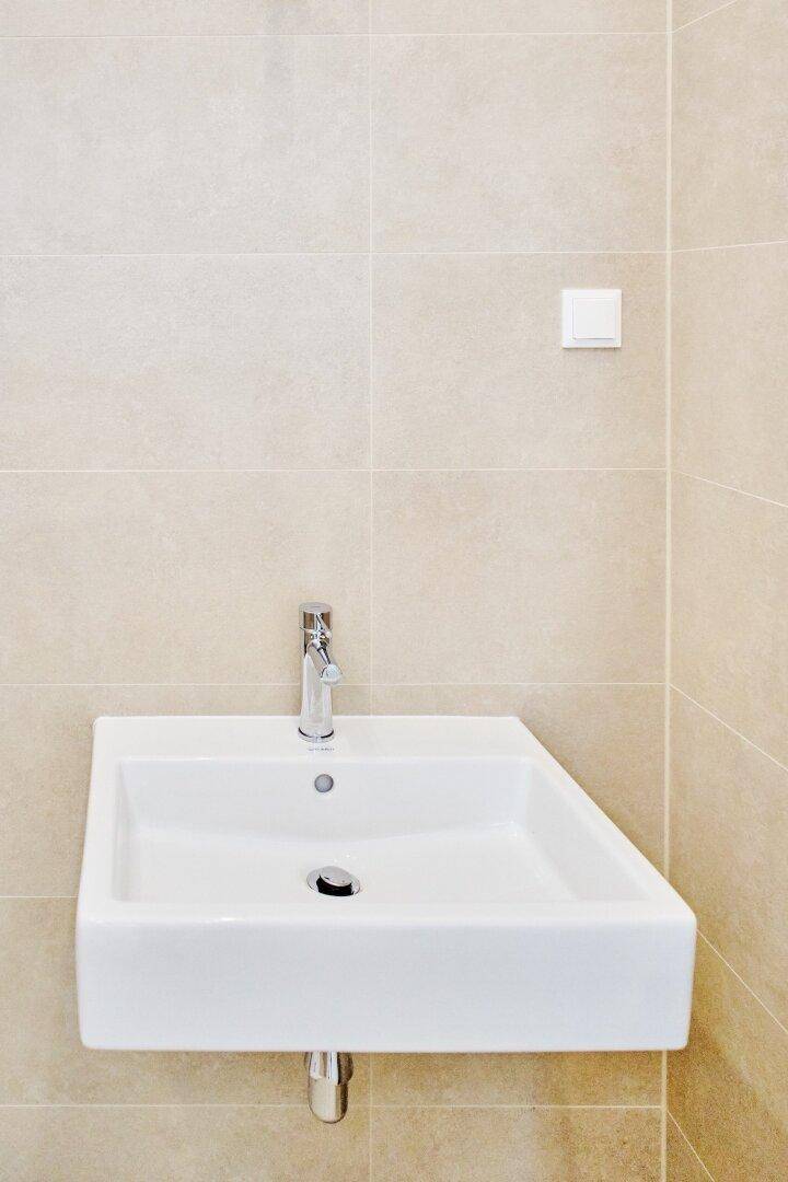 Modernes Wandwaschbecken mit Chromarmatur und hellen Fliesen im Badezimmer.