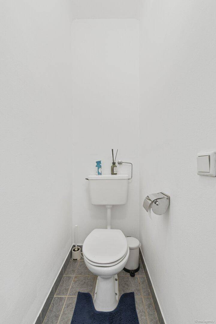Schlichtes Gäste-WC mit Stand-WC und Fliesenboden in neutralen Farben.