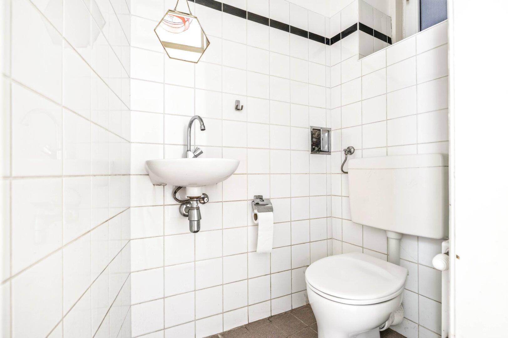 Eine kleine Gästetoilette mit weißen Fliesen, einem Waschbecken und einer Toilette.