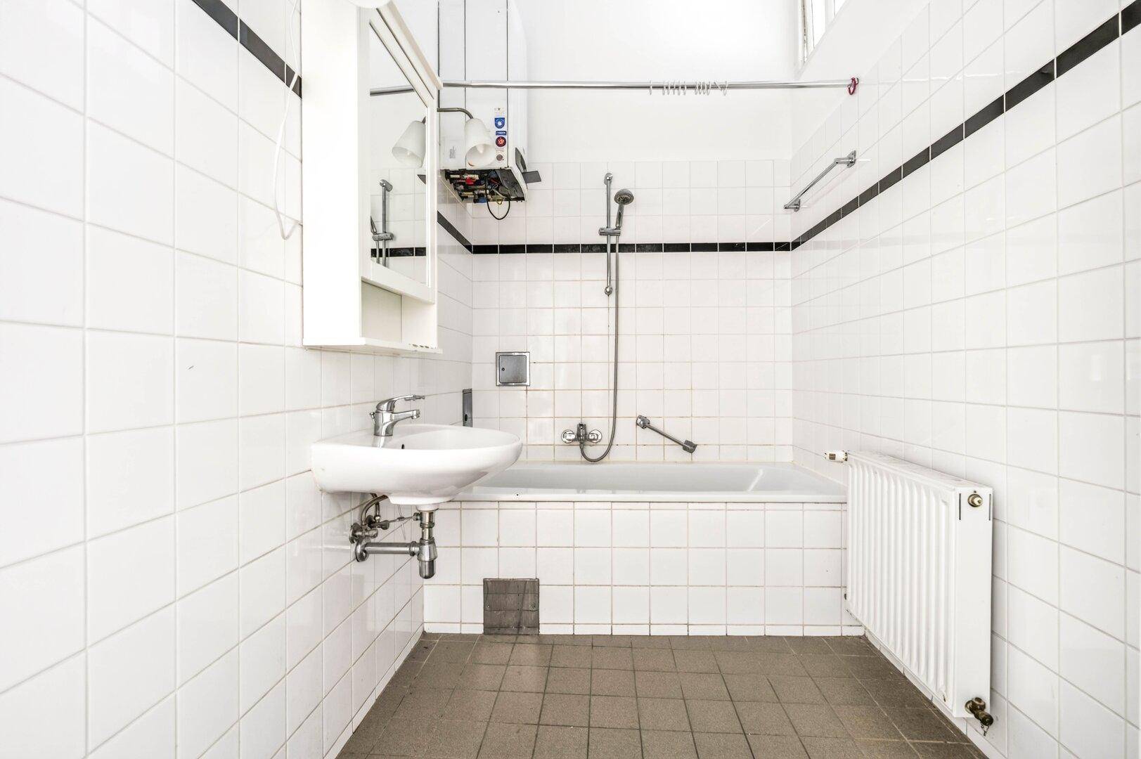 Ein Badezimmer mit weißen Fliesen, einer Badewanne mit Duschfunktion und einem Waschbecken.