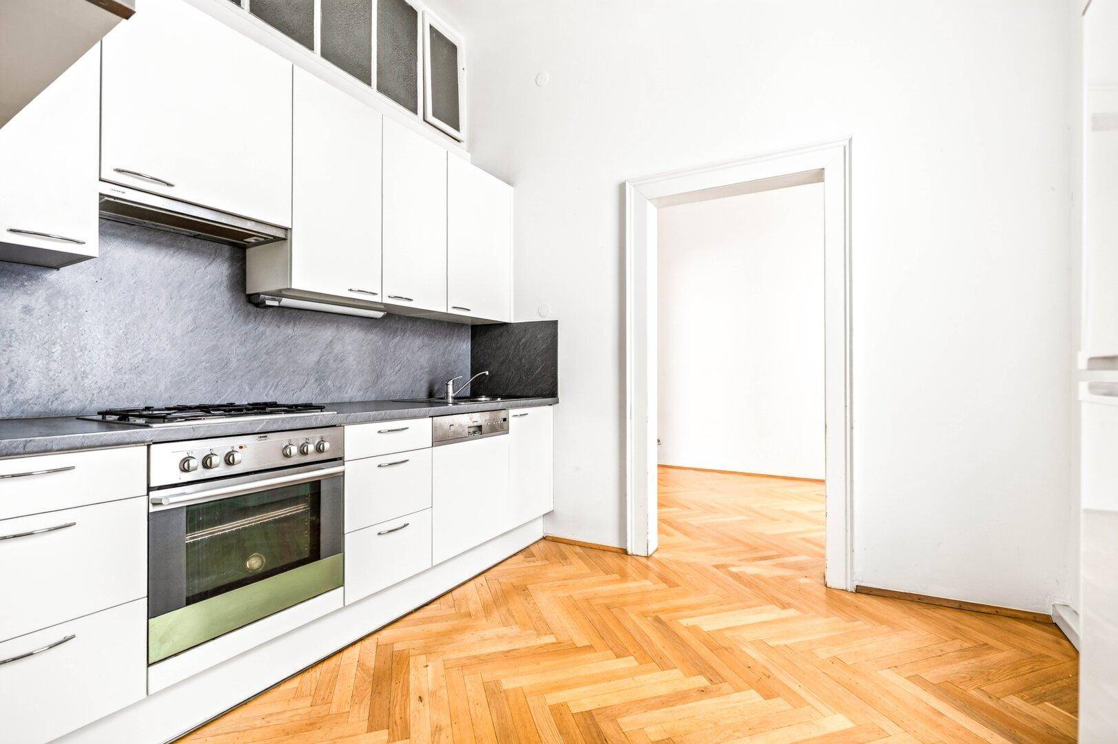 Eine moderne Küche mit weißen Schränken, einem Backofen, einem Geschirrspüler und dunkler Arbeitsplatte.