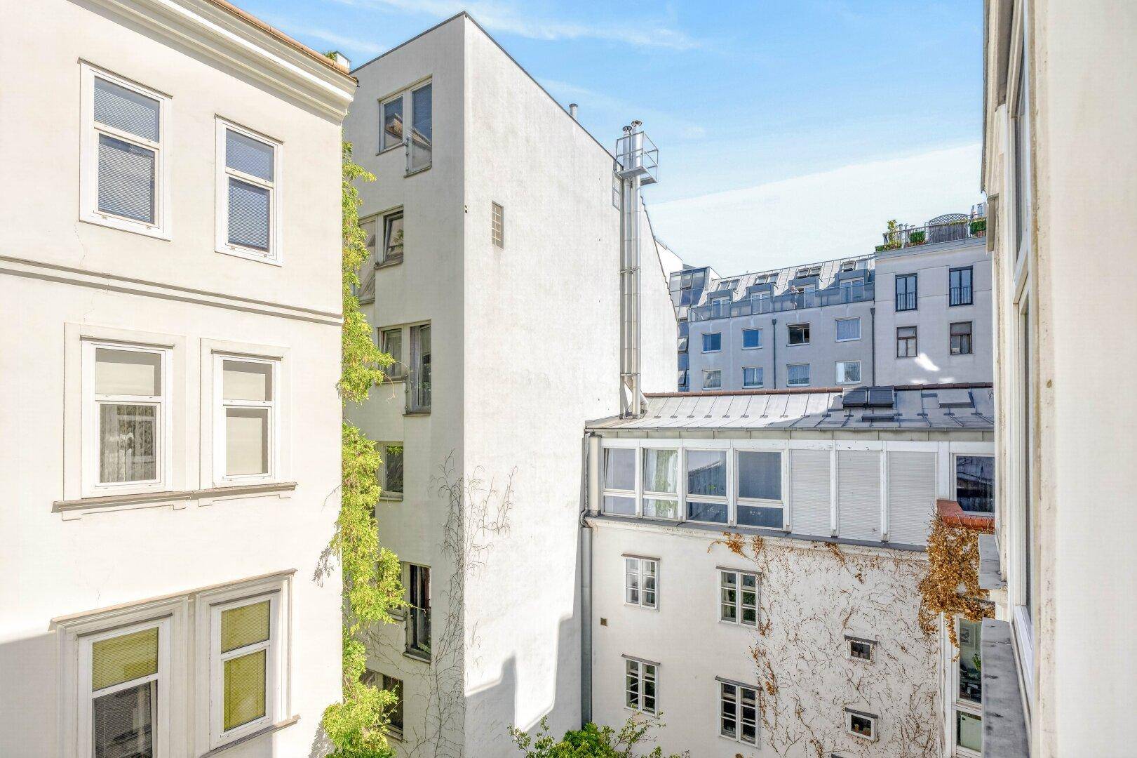 Eine Ansicht von Gebäudefassaden mit vielen Fenstern und begrünten Wänden unter blauem Himmel.