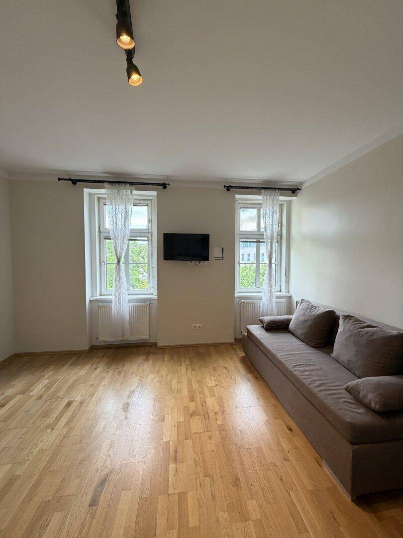 Gemütlicher Wohnbereich mit Sofa, zwei Fenstern und hellem Parkettboden.