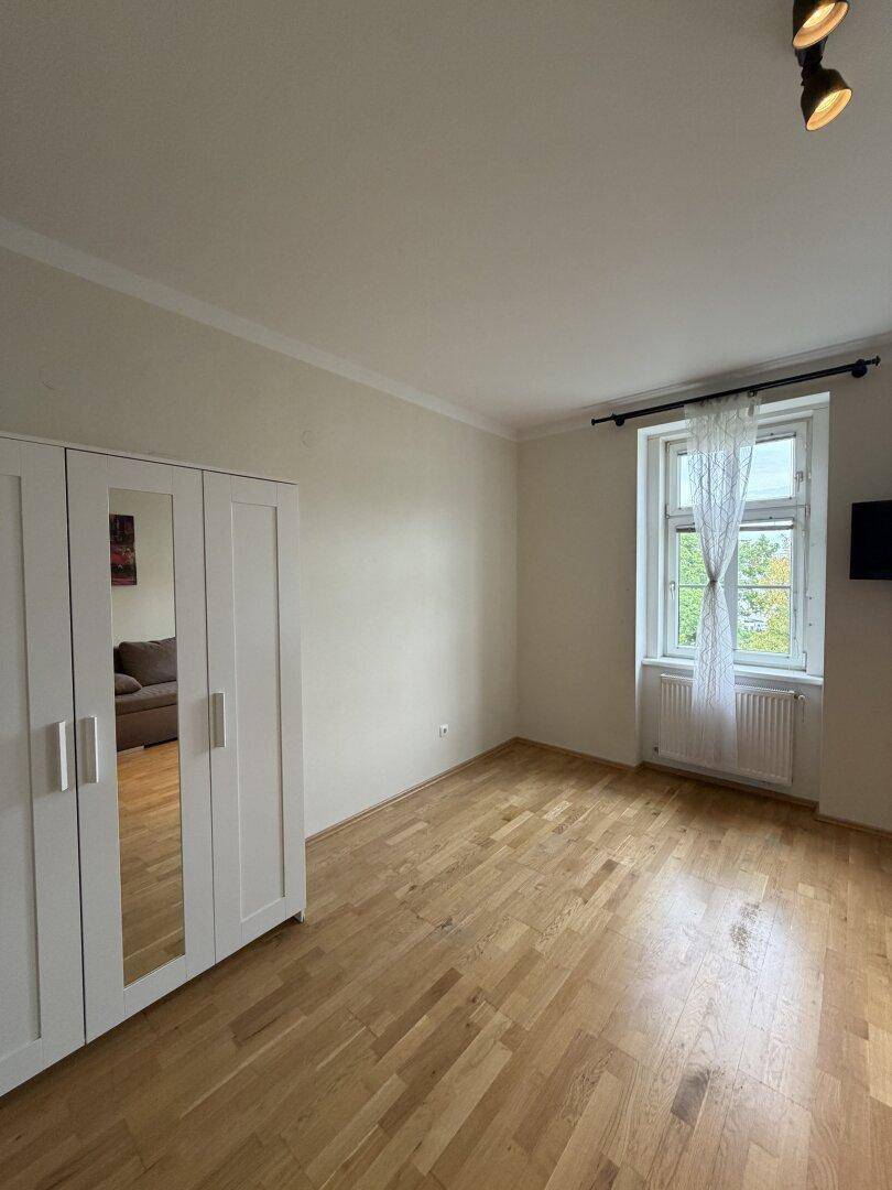 Heller Wohnraum mit großem Kleiderschrank und Fenster mit Blick ins Grüne.