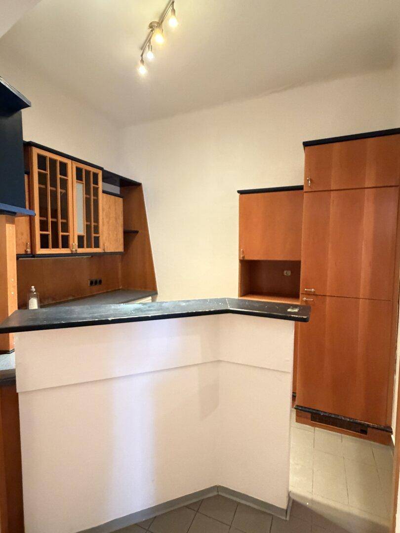 Kleine Küche mit älteren Holzschränken, dunkler Arbeitsplatte und integrierter Bar.