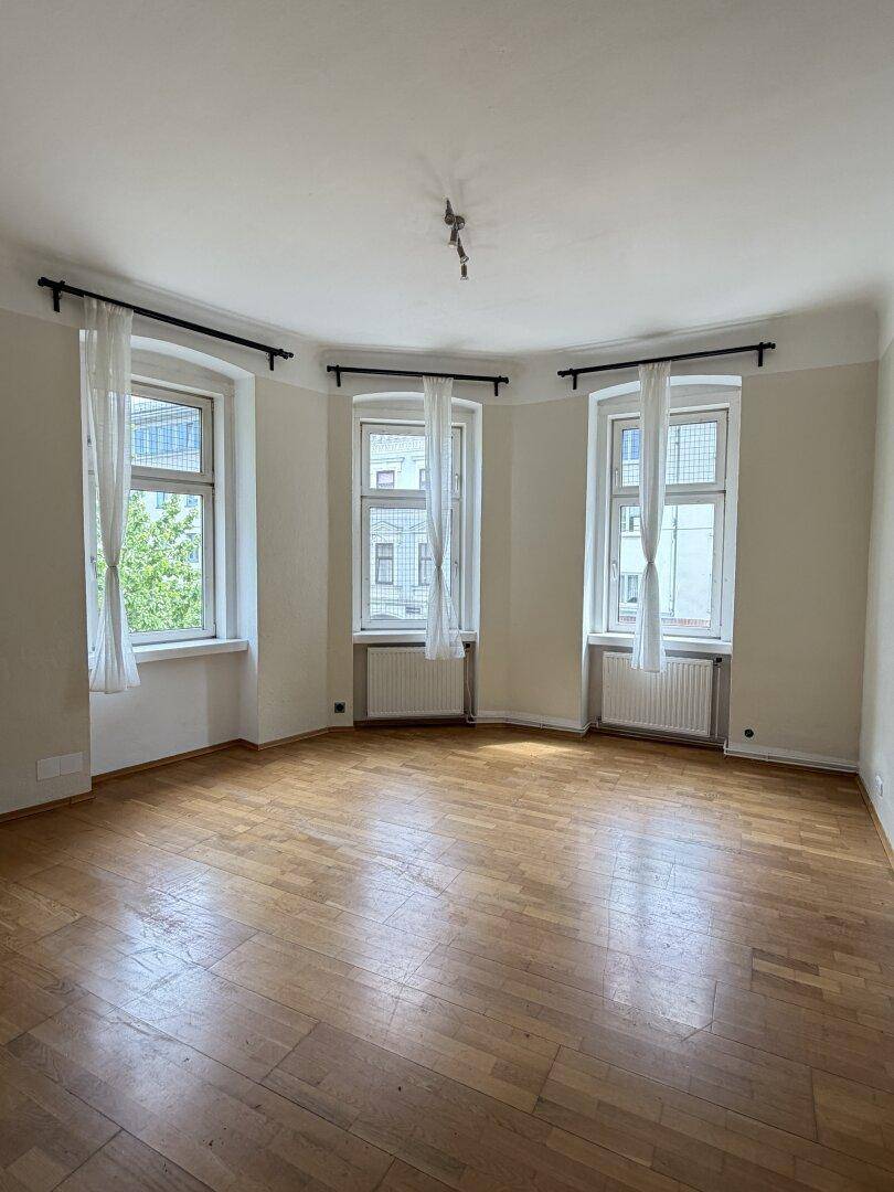 Geräumiges Wohnzimmer mit Parkettboden und drei großen Fenstern für viel Helligkeit.