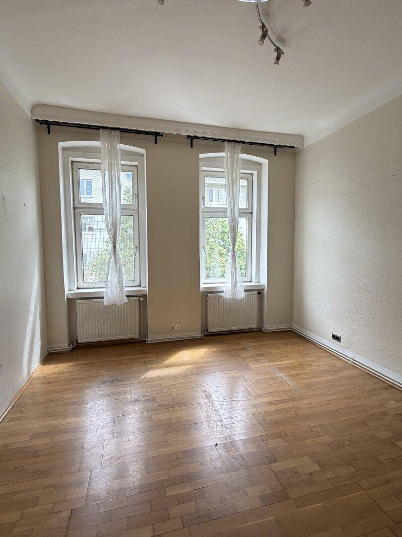 Helles Schlafzimmer mit Parkettboden und zwei Fenstern, die viel Tageslicht bieten.