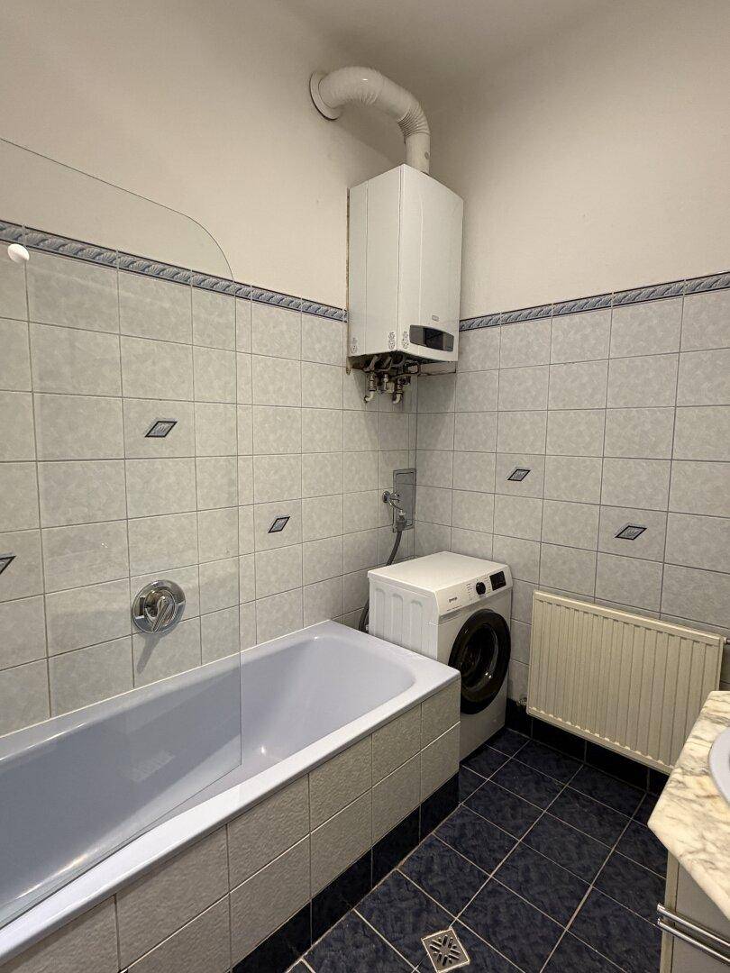 Badezimmer mit Badewanne, Waschmaschine und Gastherme, gefliest in hellen Farben.