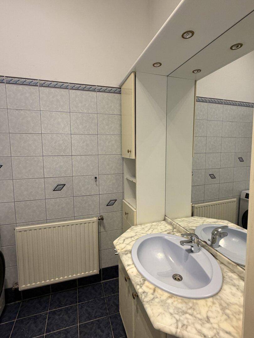 Badezimmer mit Waschbecken, Spiegel und Marmor-Waschtisch, gefliest in hellen Farben.