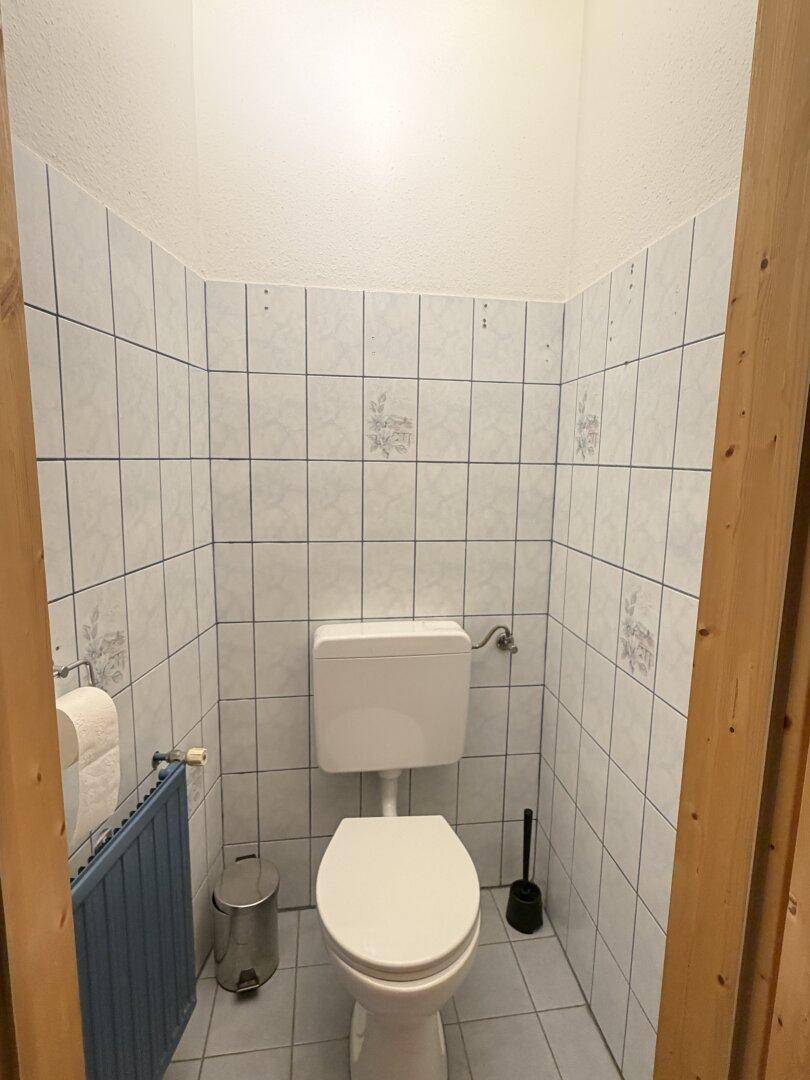 Separates WC mit hellen Fliesen, Toilette und Heizkörper, funktional und sauber.