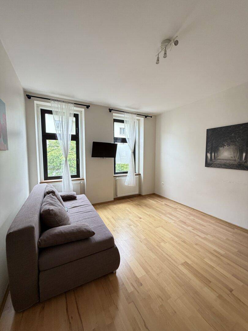 Gemütliches Wohnzimmer mit Sofa, Holzboden und zwei Fenstern für natürliches Licht.