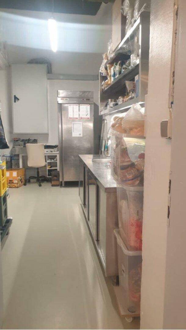 Lager- und Vorbereitungsbereich einer Großküche mit Edelstahlmöbeln und einem großen Kühlschrank.