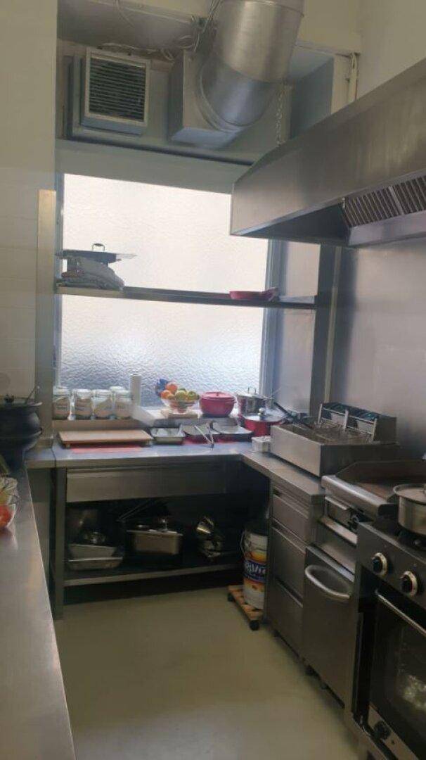 Professionelle Großküche mit Edelstahlgeräten, Abluftsystem und einem Fenster für Tageslicht.
