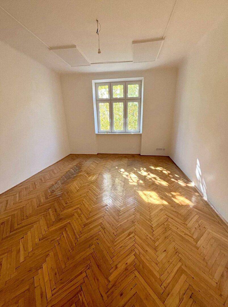 Helles Zimmer mit klassischem Fischgrätparkett und hohen Decken, ideal für vielfältige Nutzung.