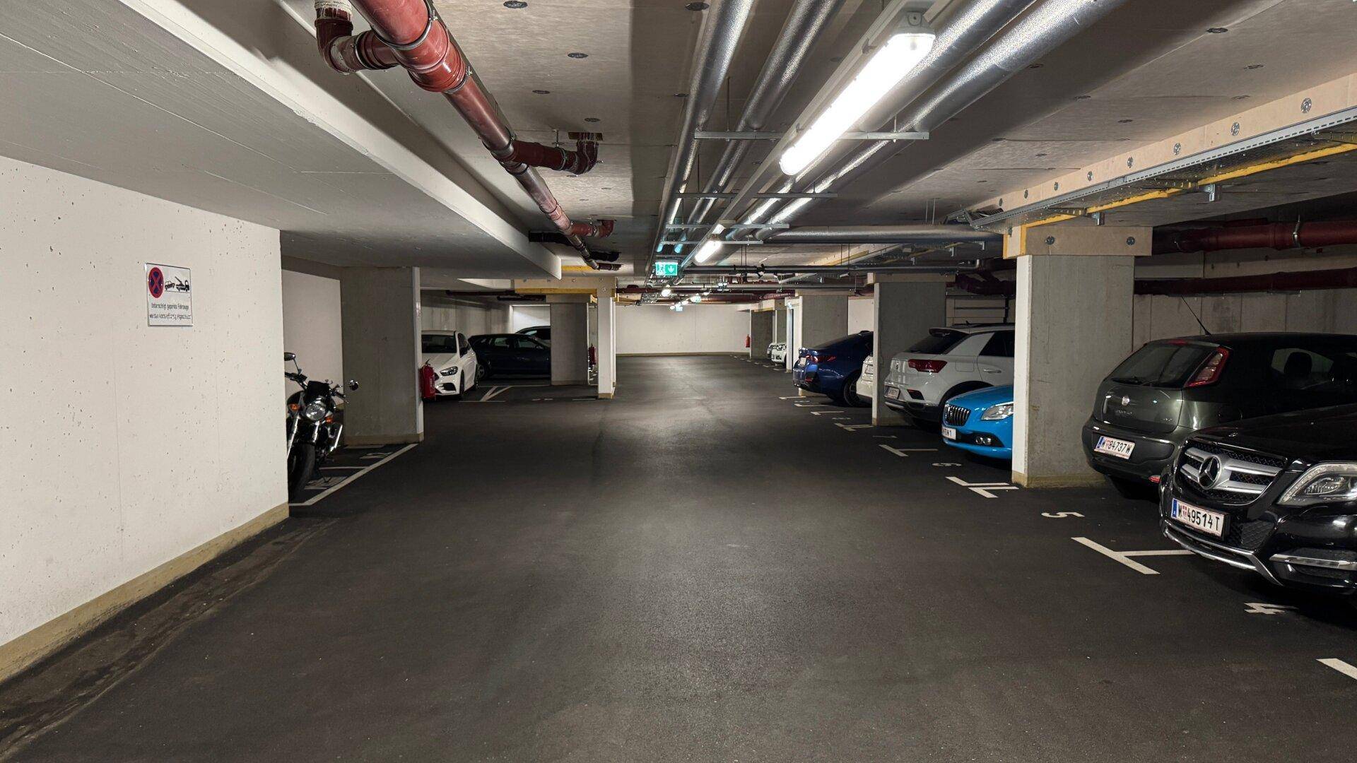 Geräumige Tiefgarage mit markierten Stellplätzen, sichtbaren Leitungen und Beleuchtung.