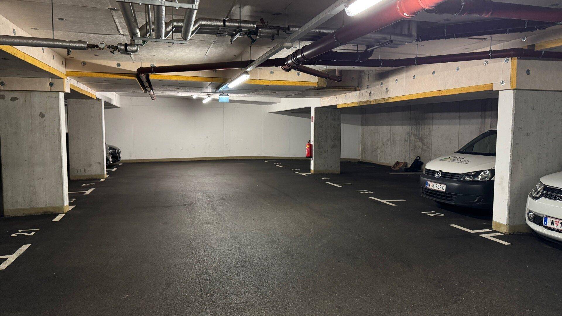 Weitläufige Tiefgarage mit vielen freien Stellplätzen, Betonstützen und Deckeninstallationen.