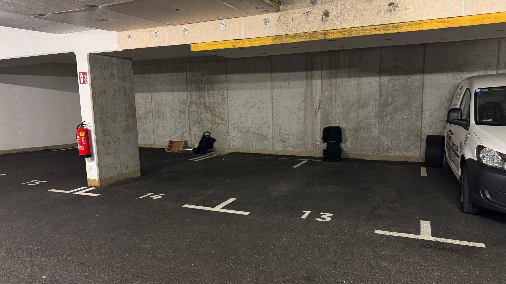 Nahaufnahme von nummerierten Stellplätzen in der Tiefgarage mit Betonwänden und Feuerlöscher.
