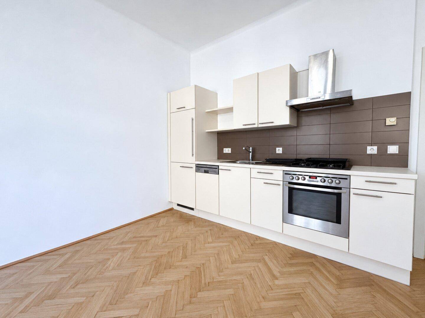 Moderne Einbauküche mit hellen Schränken, Gasherd und integrierten Geräten auf Fischgrätparkett.
