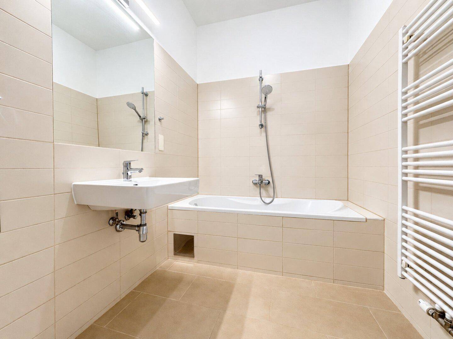 Modernes Badezimmer mit beigefarbenen Fliesen, Badewanne mit Dusche und beheiztem Handtuchhalter.
