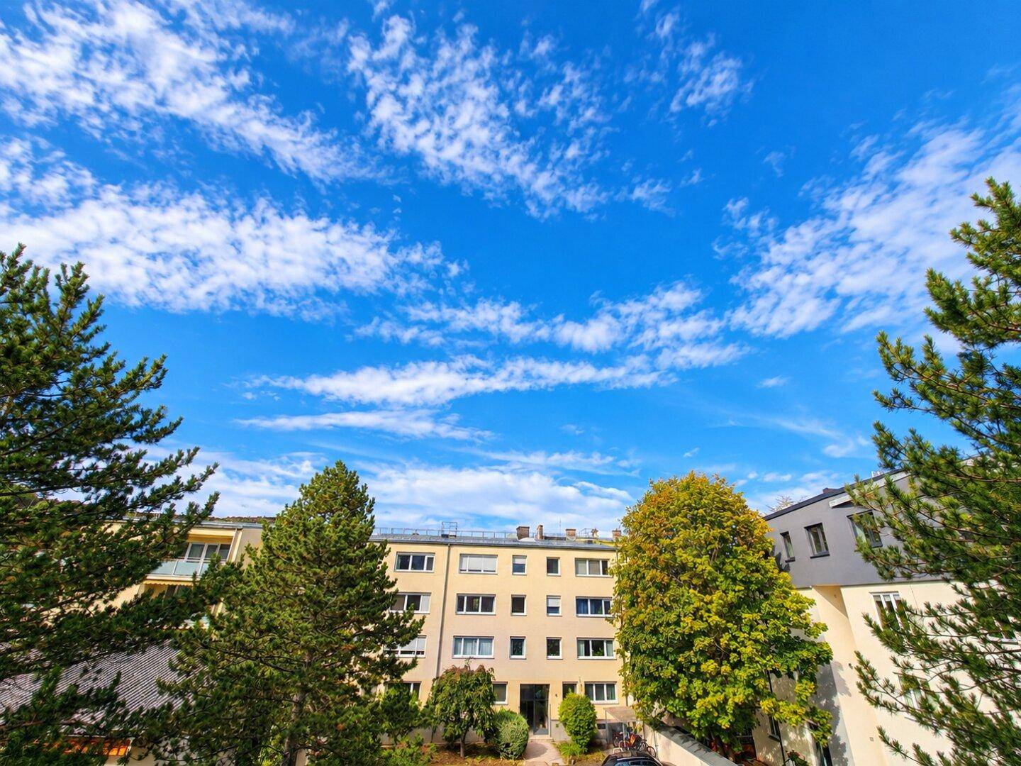 Mehrfamilienhaus mit grüner Umgebung und Bäumen unter einem strahlend blauen Himmel.