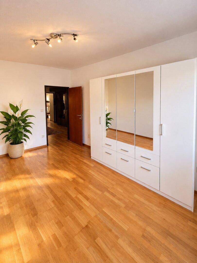 Helles Schlafzimmer mit Parkettboden und großem Spiegelschrank, durchflutet von Sonnenlicht.