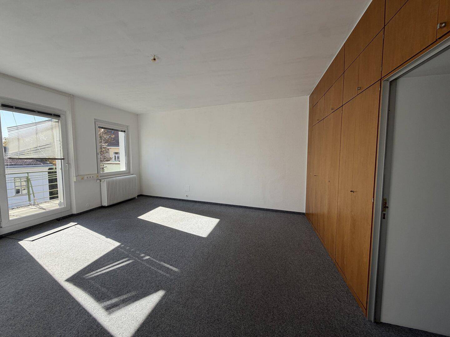 Heller Raum mit grauem Teppichboden und einer Wand aus integrierten Holzschränken.