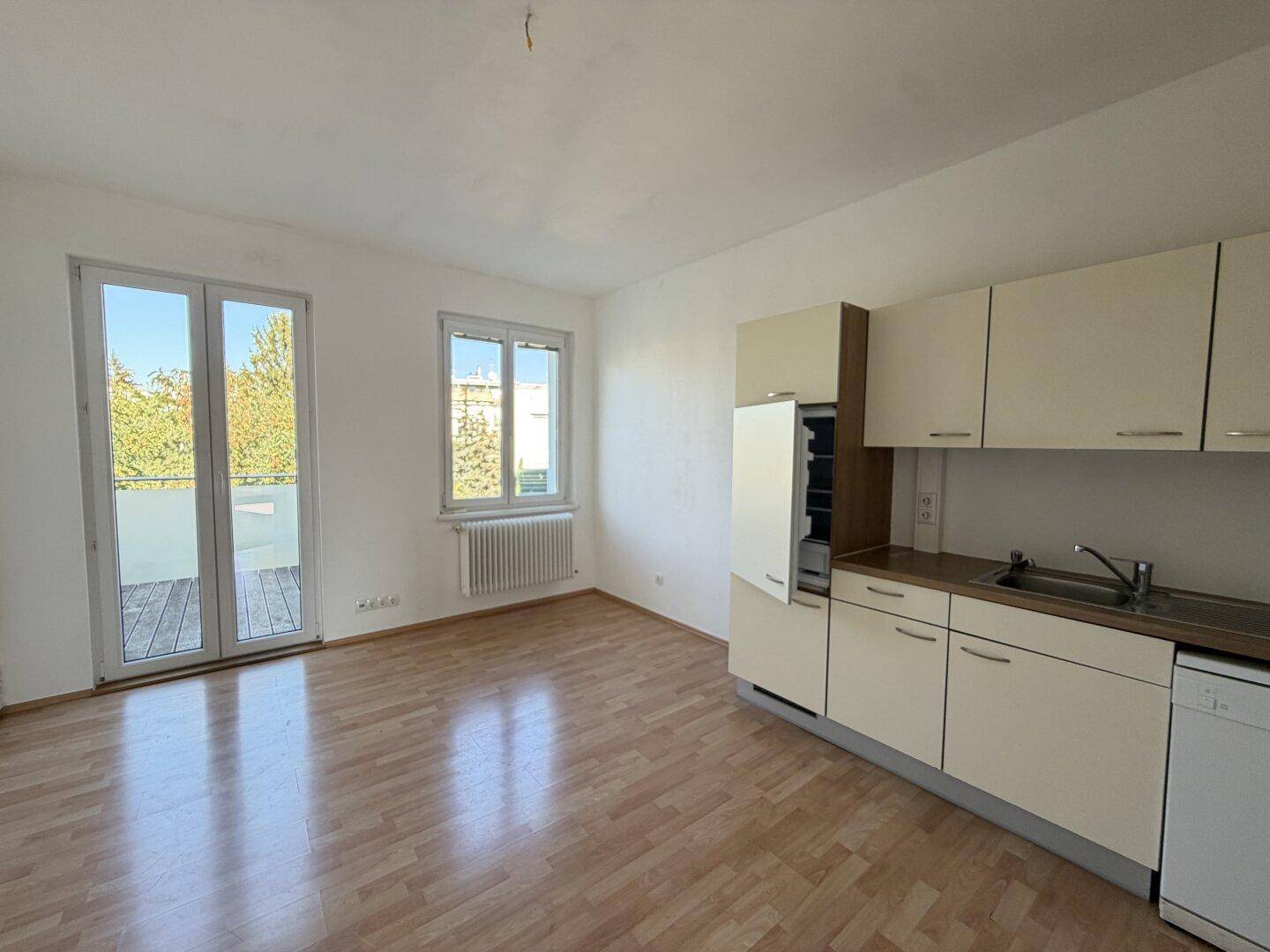 Heller Raum mit Kochnische, Holzboden und Zugang zu einem Balkon oder einer Terrasse.