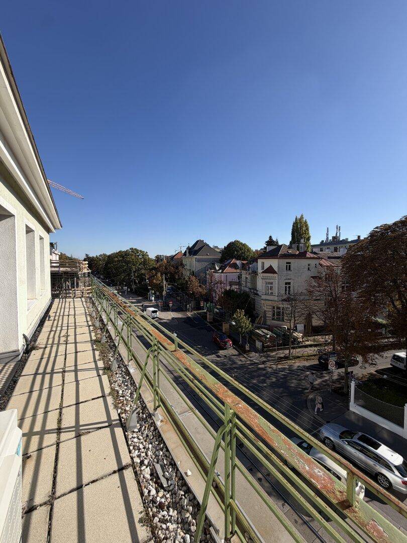Langer Balkon mit Blick auf die Straße und die umliegenden Gebäude unter blauem Himmel.