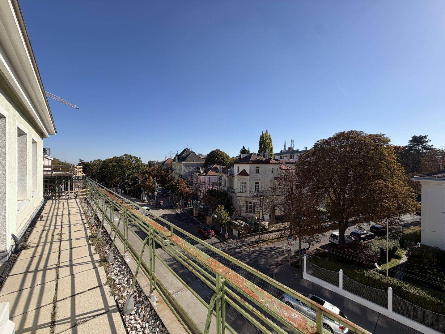 Langer Balkon mit Blick auf die Straße und die umliegenden Gebäude unter blauem Himmel.