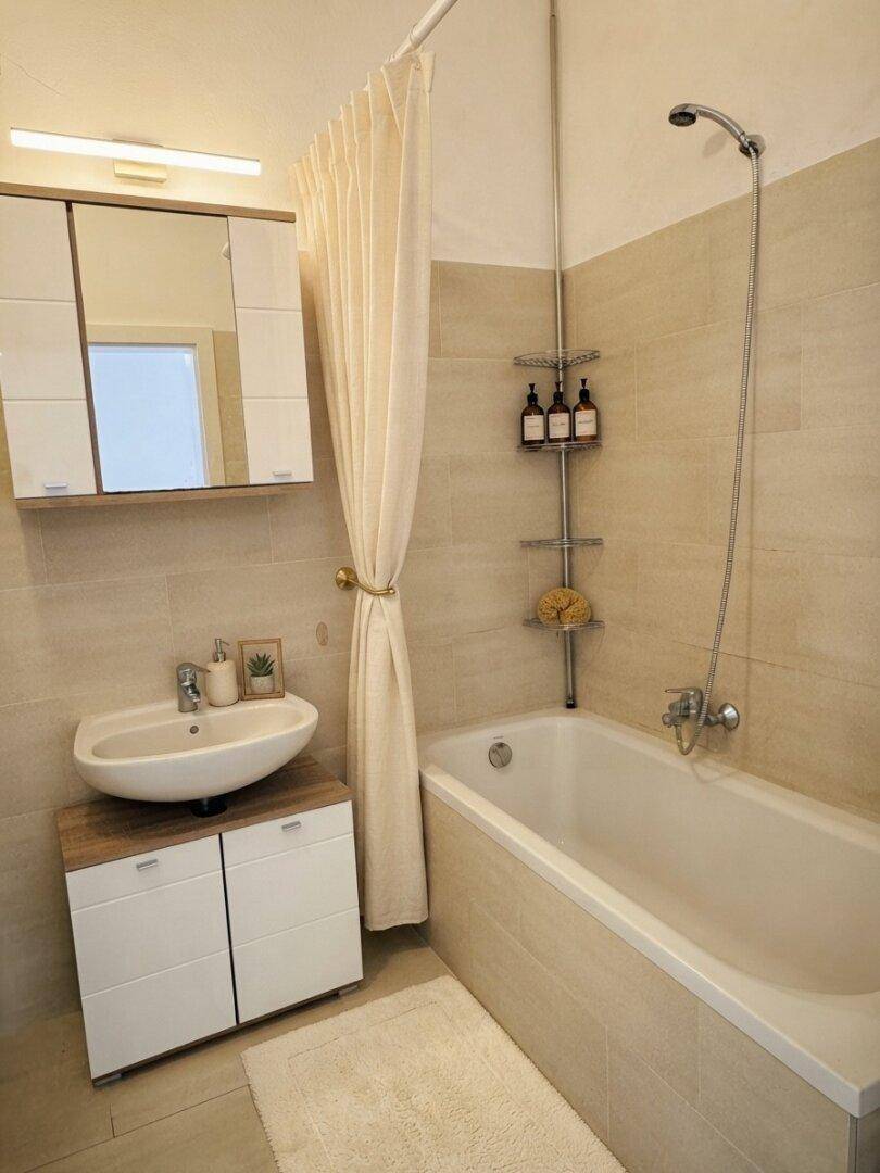 Modernes Badezimmer mit Badewanne, Duschvorhang, Einzelwaschbecken und Spiegelschrank.