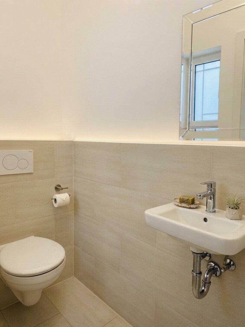 Kleines Gäste-WC mit wandhängender Toilette und kompaktem Waschbecken, hell gefliest.