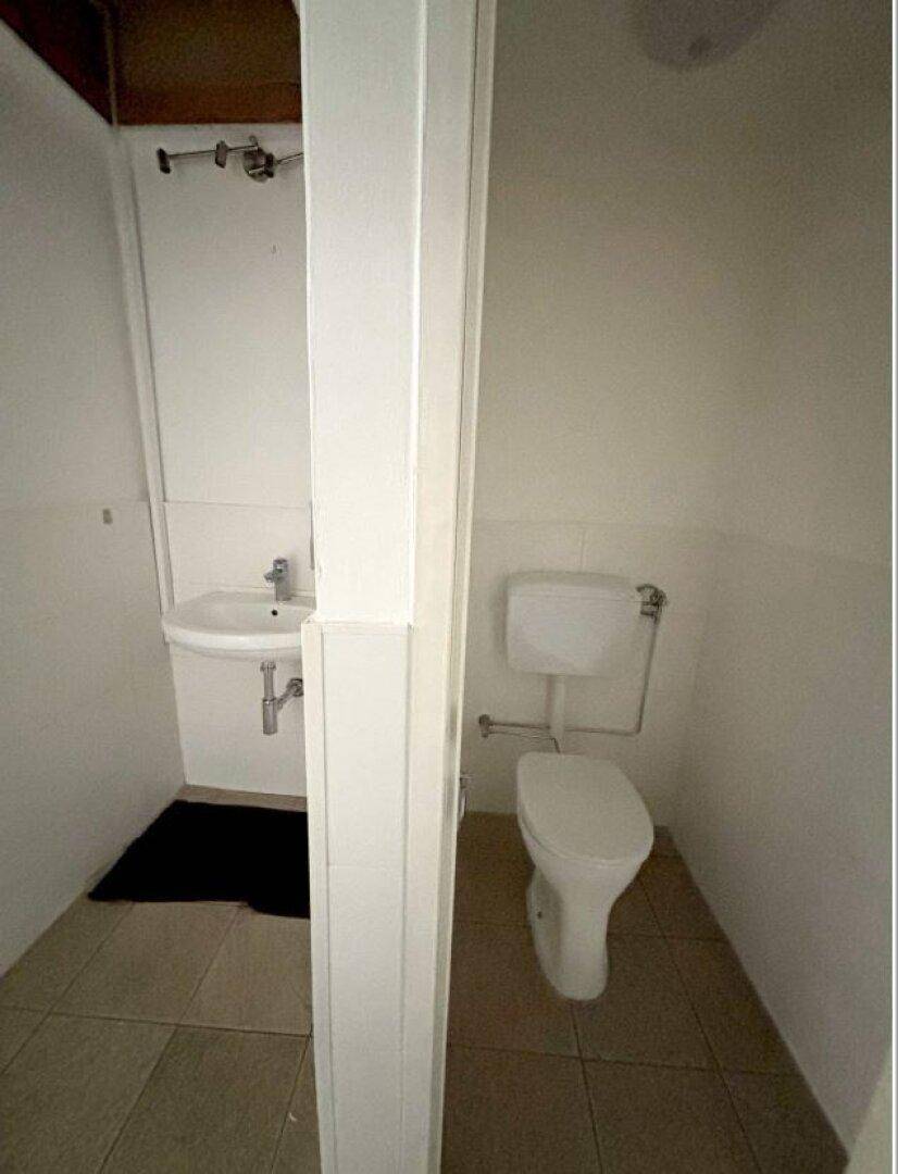 Einfache Toilette mit Waschbecken und Fliesenboden in einem kleinen Raum.