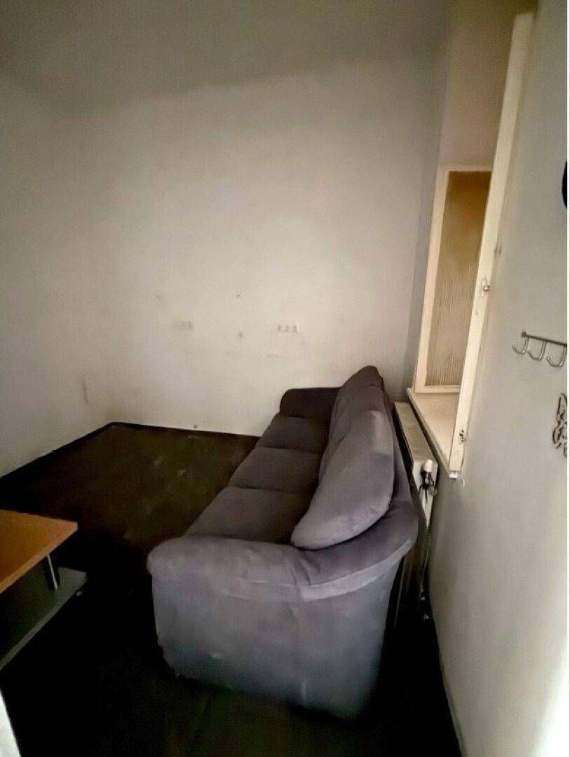 Kleiner Wohnbereich mit einem grauen Sofa und einem Fenster mit Heizkörper darunter.