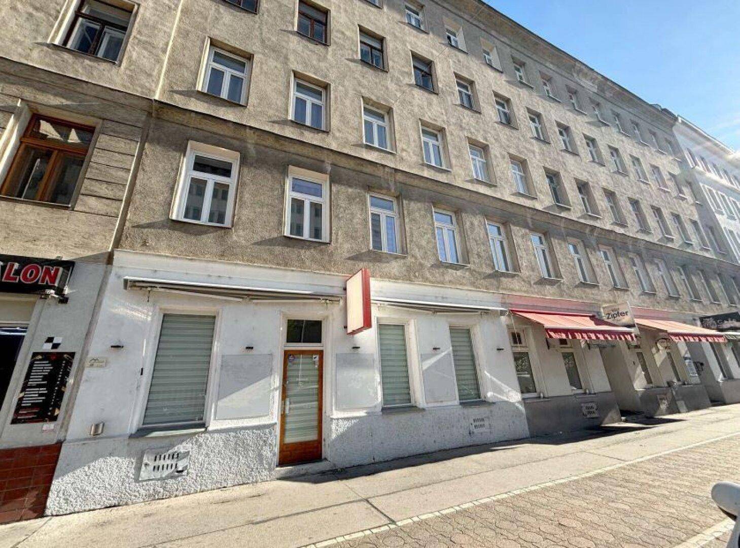 Altbau-Fassade mit Ladenlokalen im Erdgeschoss und Wohnungen darüber an einer Straße.