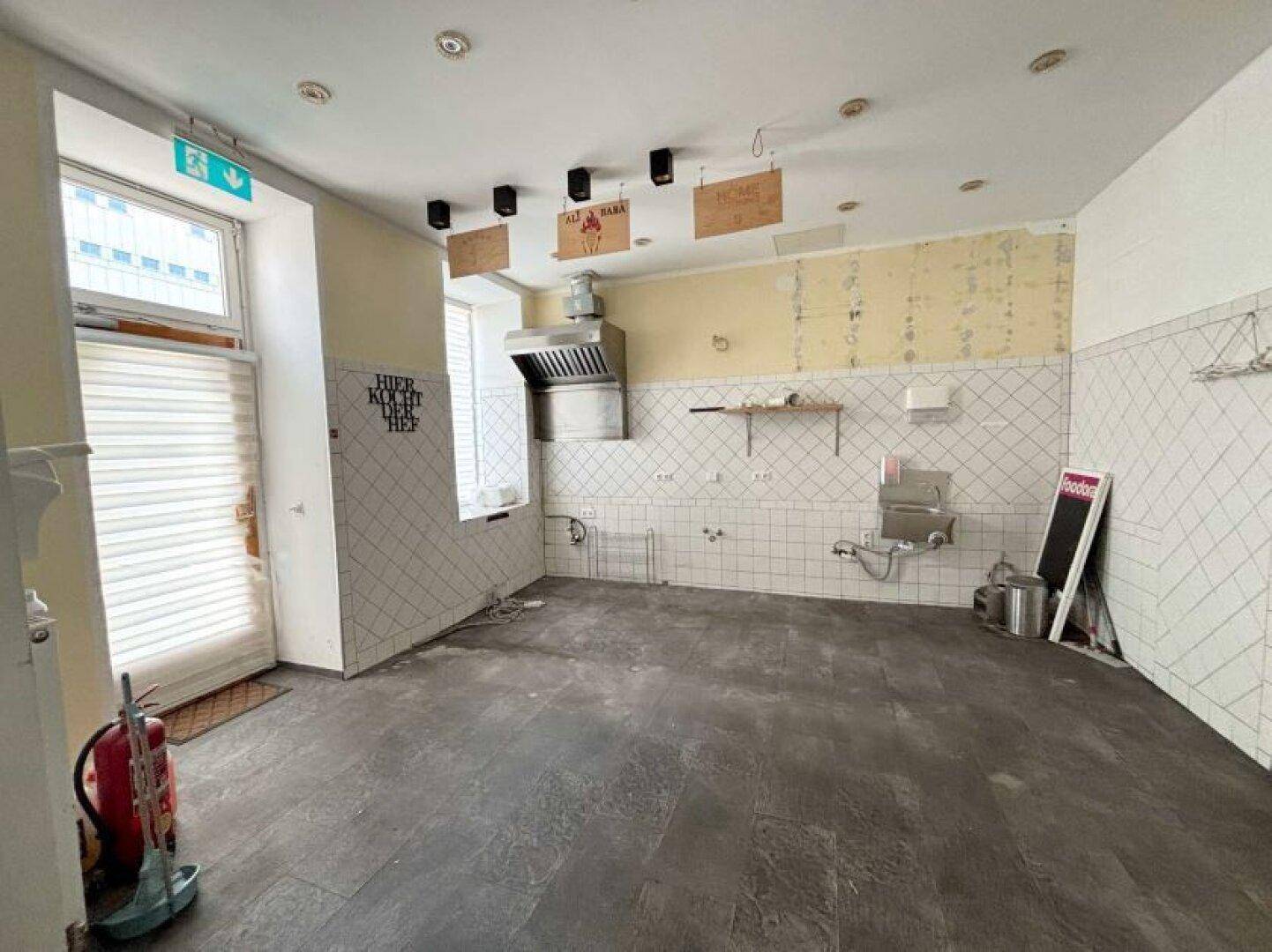 Weitläufige Gewerbeküche mit gefliesten Wänden, Dunstabzugshaube und viel Tageslicht.