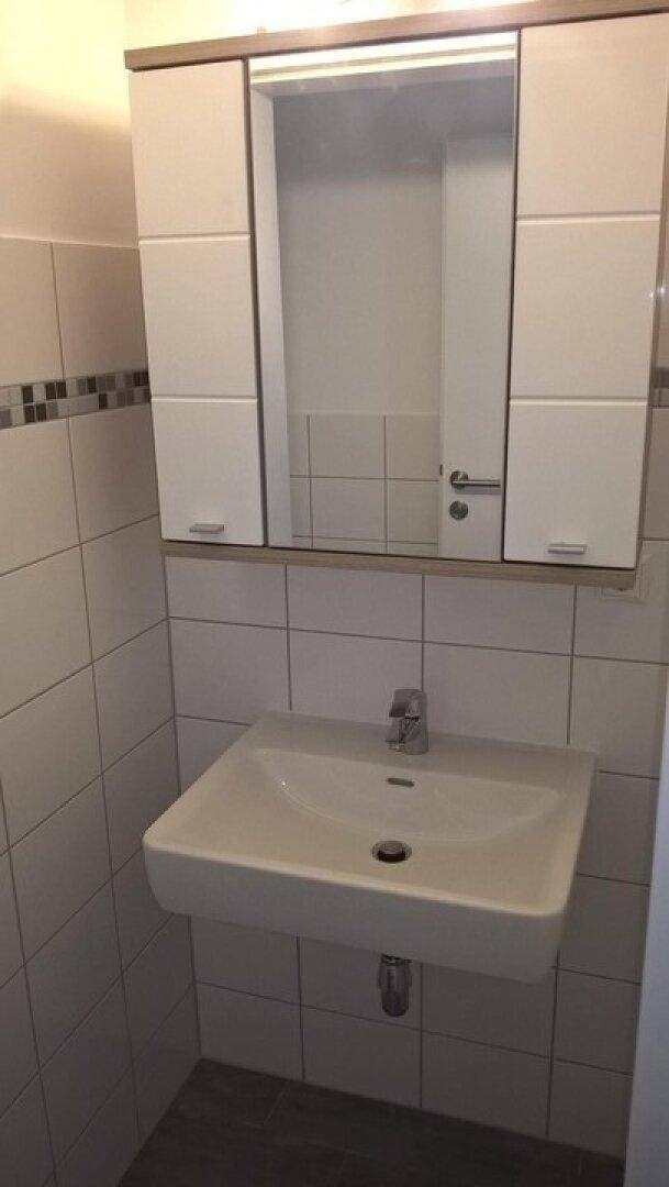 Modernes Badezimmer mit Waschbecken, Spiegelschrank und hellen Fliesen an den Wänden.
